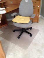 Full view of grey woven fabric office chair with yellow seat cushion on top, on carpet with clear plastic chair mat underneath. Chair visible with fabric armrests and five black wheels base.