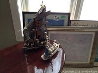 Wide angle shot showing wooden crab pot decor with directional signs and miniature fisher figurine alongside the white model fishing boat and two framed prints in the background