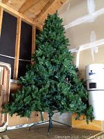 Full view of the artificial Christmas tree standing upright against a plywood wall in a garage or storage space.