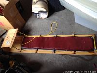 Top view of wooden toboggan showing red vinyl padded seat and yellow rope tied to the frame.