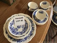 Photo showing stacked plates with blue floral pattern on white porcelain and five matching cups and saucers with blue designs and scalloped rims.