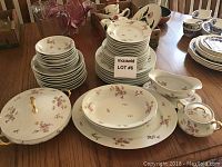 Photo showing the complete set of Limoges china including stacked plates, bowls, covered dish, large platters, and sugar bowl on wooden table.