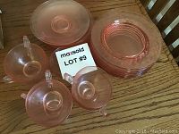 Top view of stacked pink depression glass dessert plates and saucers with three cups arranged around them on a wooden surface.