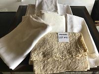 Eight folded tablecloths including a beige lace one and several white or cream linen cloths, showing vintage wear.