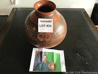 Large round burnished pottery vase with hand-painted traditional designs in brown and black tones, labeled Lot #24, displayed on a black surface.