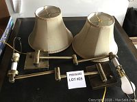 Two brass-plated wall lamps laid flat on a surface with beige pleated shades, showing both lamps disassembled with shades separate from fixtures.