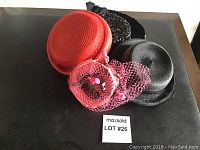 Four vintage straw hats displayed on a dark surface showing red, black, and decorative pink styles.