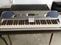 Front view of Yamaha keyboard showing full set of keys, two speakers with blue covers, and control panel.