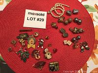 Wide view of the collection showing various pins, clip-on earrings, and pearl necklace on a red mat.