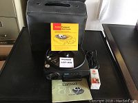 Kodak Carousel 850 projector with accessories laid out beside original carrying case, instruction manual, stack loader, and power cord.