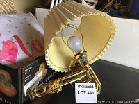 Brass plated wall lamp with pleated cream-colored lampshade visible with bulb in socket.