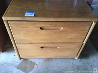 Front image of two-drawer oak file cabinet with locking mechanism and attached lot label.