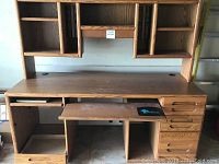 Front view of the large oak desk with hutch, showing desktop surface, multiple shelves, drawers, and keyboard tray.