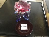 Photo showing two cranberry glass duck figurines on top of a cranberry glass dessert plate on a black surface.