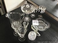 Photo showing an assorted collection of clear glassware including two vintage wine glasses, a cut glass candy dish, two glass candle holders with hanging droplets, a small dish, pitcher, and small decorative glass pieces.