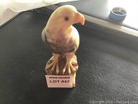 Front view of alabaster eagle sculpture showing its detailed carving, painted eyes and beak, sitting on a textured base with visible repair marks.