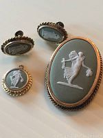 Set of a brooch, pendant, and earrings featuring Wedgwood jasperware design in white on green background with twisted metal borders.