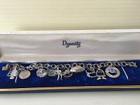 Full view of the sterling silver charm bracelet with multiple charms including colorful stones and enamel badges inside a Dynasty jewelry box.