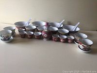 Full view of the tea set and soup bowls arranged in a row on a light surface showing 21 pieces including tea cups, bowls, soup spoons, and a lidded pot.