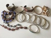 Overview of fifteen bracelets including various metal bangles, copper cuffs, linked bracelets, and beaded types.