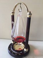 Front view of the weather glass barometer and thermometer showing clear glass vessel with red liquid and dark wood columns with gold accents