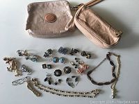 Full view showing two beige leather Roots pouches and assorted costume jewellery pieces laid out on a flat surface