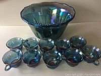 Full view of the blue iridescent Carnival Glass punch bowl with ten matching cups arranged in front.