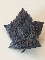 Front view of WWII cap badge shaped as a maple leaf with crown, shield, and text indicating The Duke of Connaught's Own Overseas Battalion 158, Canada.