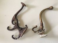 Top view of two antique brass wall hat holders showing their length, shape, and overall condition including paint residue and wear.