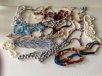 Overhead view of nineteen assorted costume jewelry necklaces laid out, showing various bead, pearl, and floral designs.