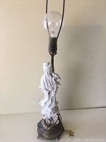 Full view of antique lamp showing porcelain Kwan-Yin figure and metal base with exposed bulb and harp.