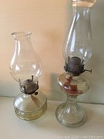 Two antique glass oil lamps, one featuring a ribbed glass base and Queen Mary burner, the other with a smooth glass base.