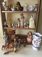 Photo showing three shelves filled with approximately three dozen collectible ceramic, wooden and pottery figurines. Items include various dolls, animals, pottery vases and small decorative pieces.