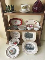 The full set of china and ceramic pieces arranged on a shelf for display showing plates, teacups, saucers, and decorative ceramics.