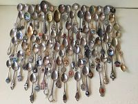 Photo showing a wide assortment of over seventy-five collectible spoons and a few forks with diverse decorative handles, including enamel crests and metal engravings