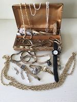 Full view of costume jewellery collection with various necklaces, bracelets, earrings, and two watches laid out in front of an open vintage jewelry box.