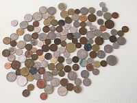 Over 100 world coins of varied sizes, metals, and origins spread on a white surface showing a diverse collection.