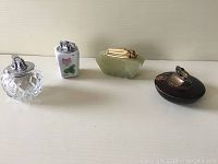 Front view of four vintage table lighters including crystal glass, ceramic with rose design, stone with metal top, and dark circular lighter