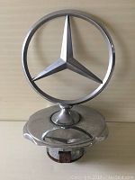 Front view of the Mercedes Benz hood ornament showing the three-pointed star in a circular frame mounted on a chrome base.