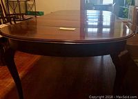 View of elongated oval wood dining table top with polished finish and minor separation marks visible on the glued sections.
