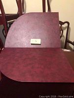 Two separated sections of a mahogany wood grain themed table pad, each fitting a part of an elongated oval dining table with dimensions approximately 84 by 42 inches. One photo shows the top surface of both sections placed side by side with rounded edge matching table shape.