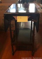 Front view of antique drop leaf tea table on wheels with lower shelf and drawer closed. Shows rectangular top with overhanging drop leaves and turned legs.