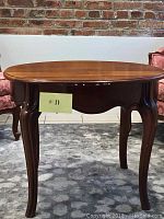 Front view of oval mahogany end table showing curved legs and polished table top.