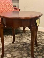 Oval shaped mahogany end table with scalloped apron and curved legs seen from a side angle.