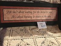 Full view of the wooden sign showing the inspirational quote 'Life isn't about waiting for the storm to pass... It's about learning to dance in the rain' with a dark wood frame.