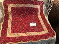 Top-down photo of square burgundy quilt with floral pattern and cream borders displayed on crocheted surface.