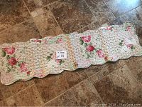 Full view of the 39x11-inch floral quilted cotton runner laid flat on tiled floor, showing scalloped edges and pink floral pattern on white background.