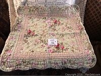 Photo of a small quilt measuring about 22x22 inches. It is made from cotton with a floral print pattern of pink and red flowers on a muted green background. Quilted with a diamond and grid stitch pattern.