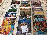 Photo showing 15 comic books arranged in two rows on a lace tablecloth, protected in clear plastic covers. Visible titles include Avengers, The Uncanny X-Men, Mystic, Titan AE, Knuckles.