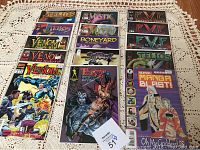 Full view of all 15 comic books in holders, arranged on a lace tablecloth, showing variety of titles including Venom, Telos, Mystic, Boneyard, Tarot, Sapphire, Super Manga Blast.